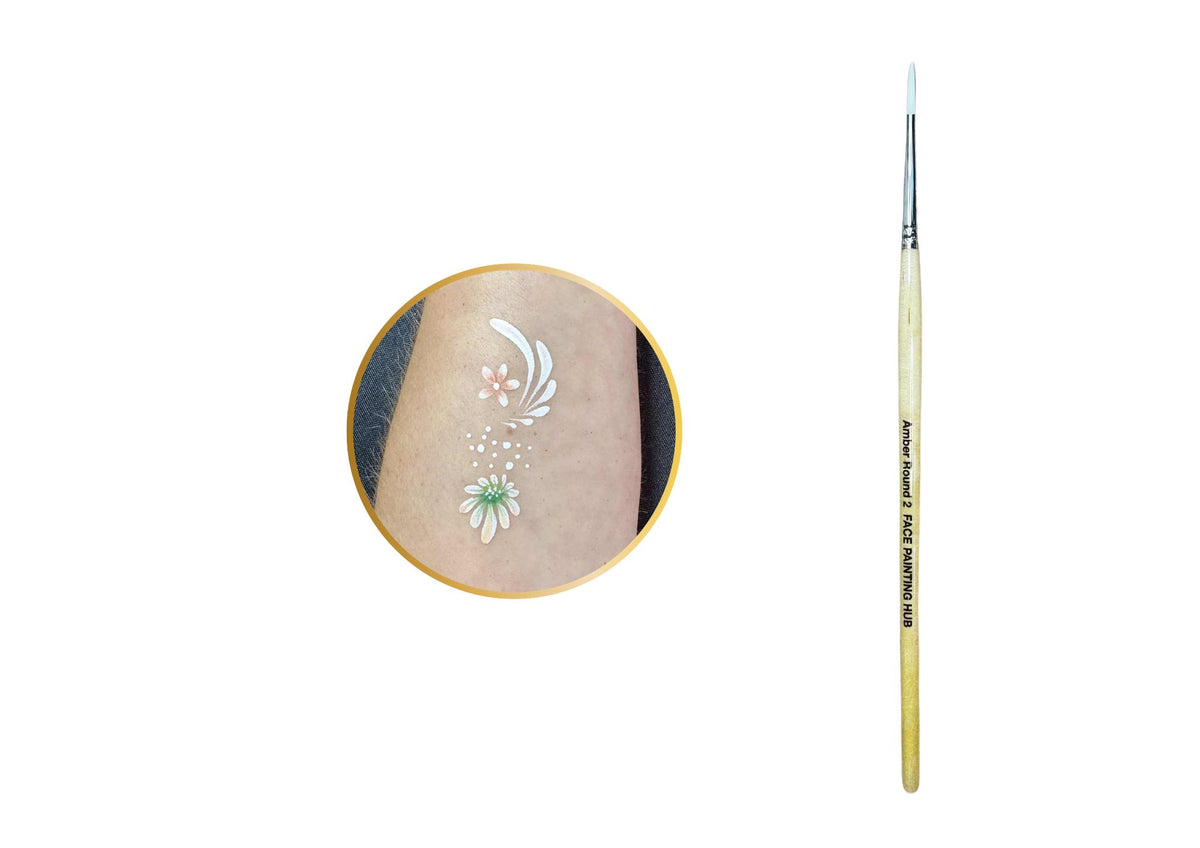 A fine-tip paint brush with a light wood handle and silver ferrule, shown next to a circular inset demonstrating a white floral body paint design on skin.